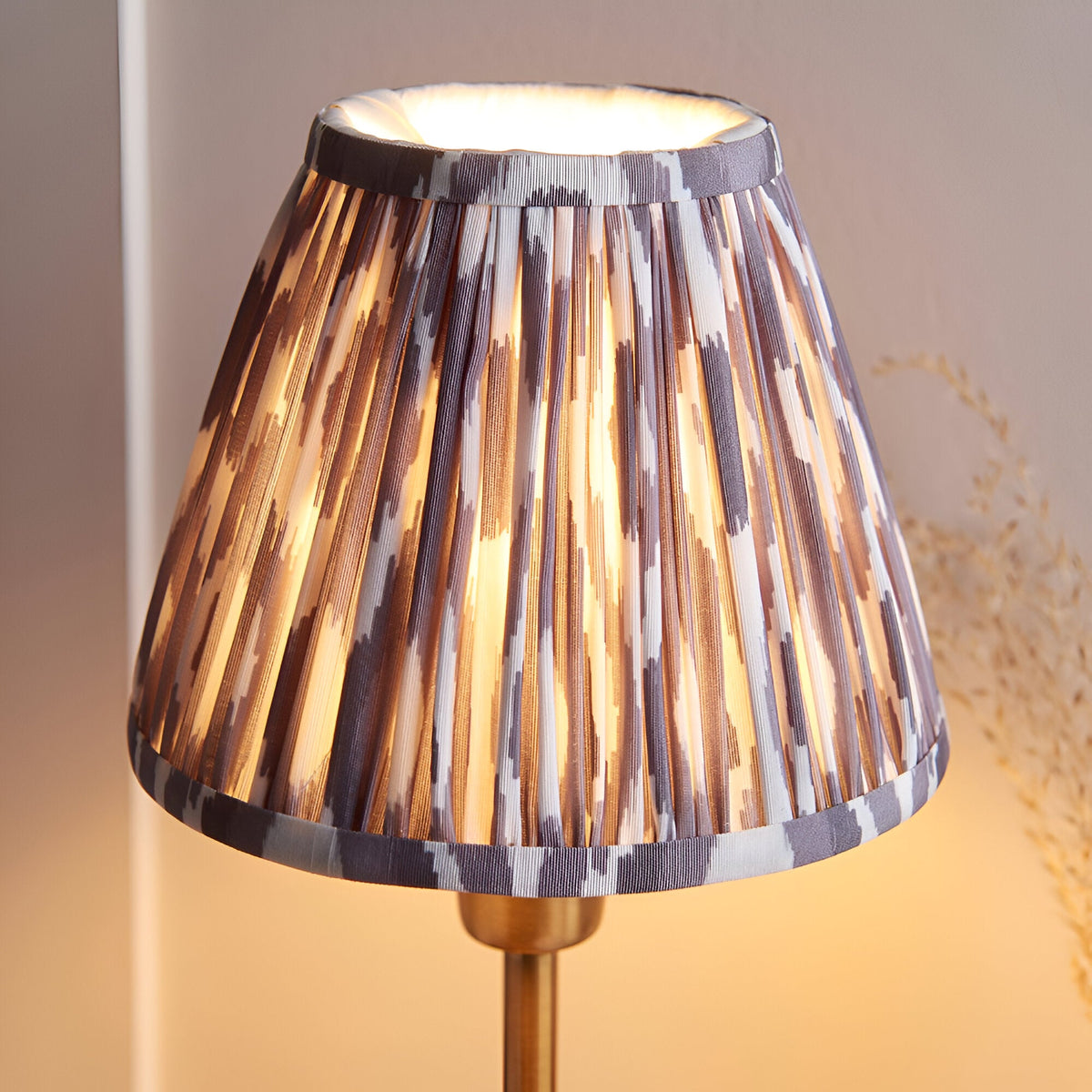 Cliffbourne Ikat Table Lamp with pleated grey-toned patterned fabric shade on a brass stepped metal base, shown lit against a neutral background.