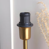 Close-up of the Cliffbourne Ikat Table Lamp's brass base and black E14 bulb holder, set against a light background with dried foliage.