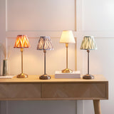 Cliffbourne Ikat Table Lamp in brass with a grey pleated fabric shade, shown among similar lamps on a wooden console table.