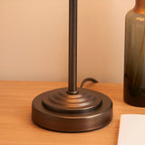 Endon Cliffbourne Zigzag table lamp base in antique bronze with stepped detailing and slim stem, shown on a wooden surface beside a green glass vase.