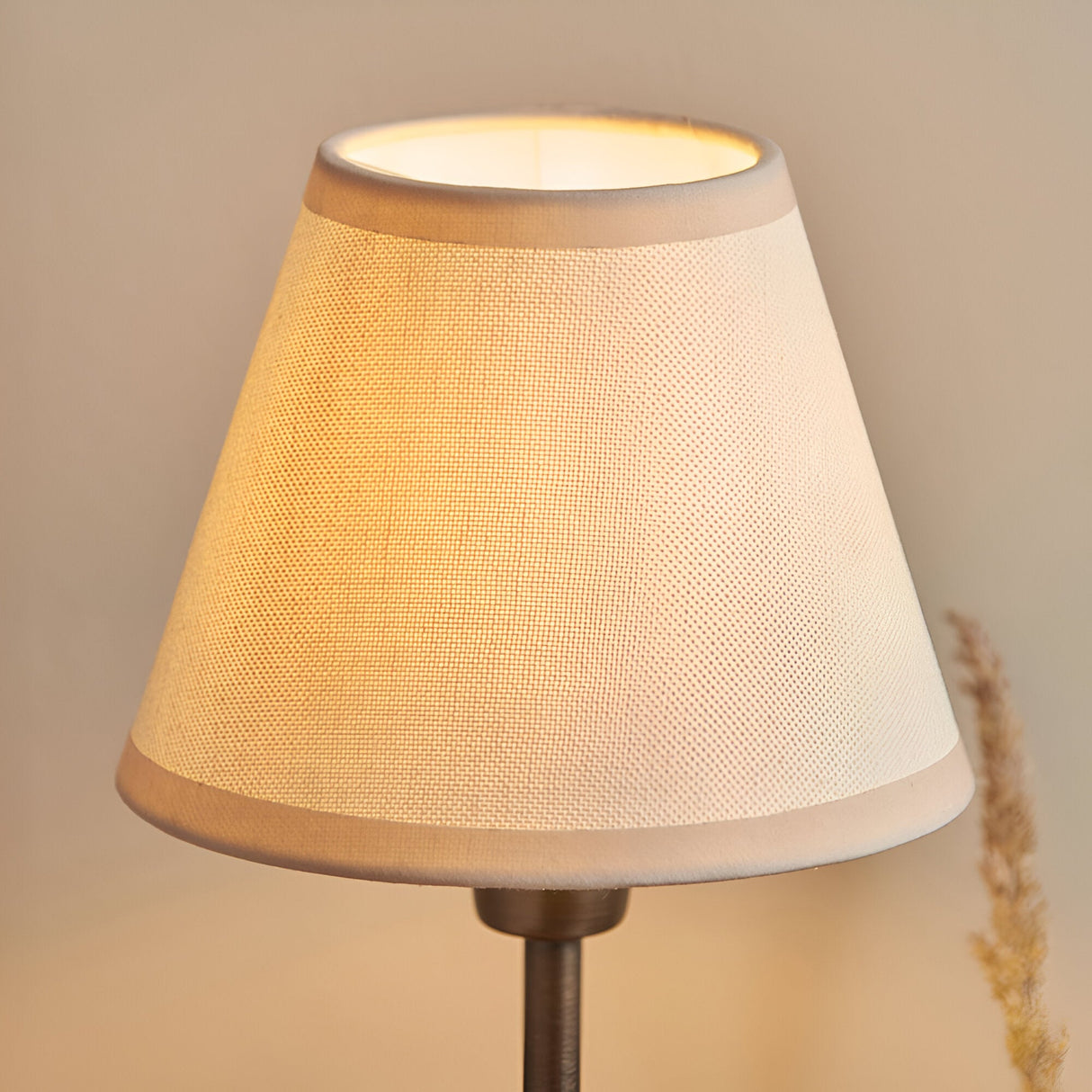 Close-up of the Endon Cliffbourne Ivy table lamp's tapered vintage white cotton shade with almond taped edge, lit on a bronze stem.