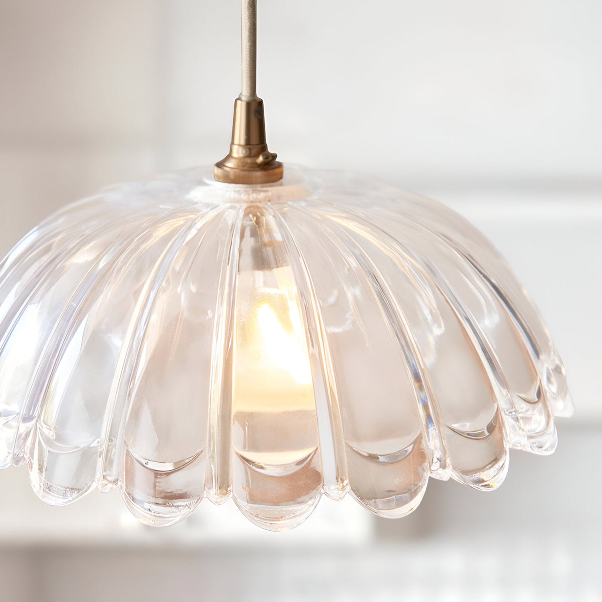 Endon Brackmont Carnation pendant light with a heavy clear glass domed scalloped shade and brushed aged brass fitting, illuminated by a single B22 lamp.