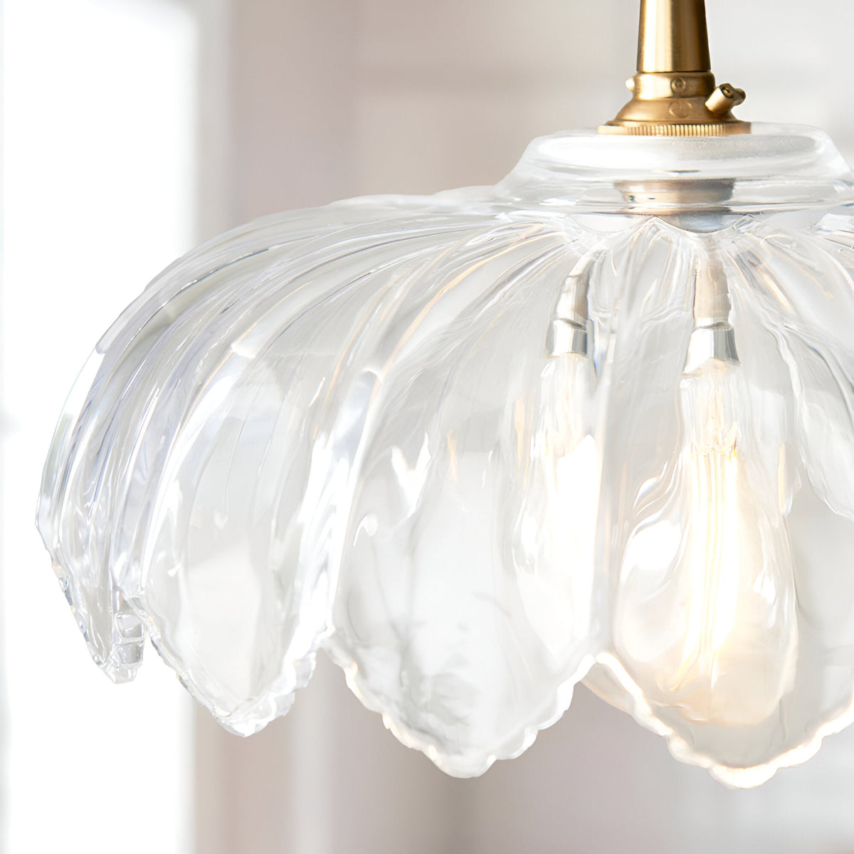 Close-up of the Brackmont Camellia Pendant showing its scalloped clear glass shade and brushed brass fitting with a warm glowing bulb.