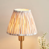 Endon Cliffbourne Ikat table lamp lit on a brushed brass stepped base with a pleated tapered faux silk shade in grey and natural ikat print.