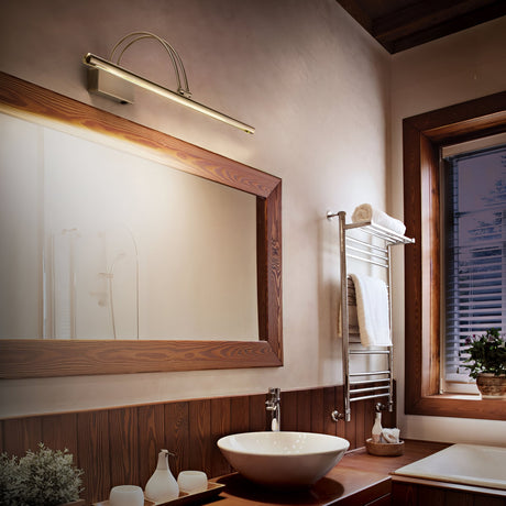 In a modern bathroom, a large wooden-framed mirror is beautifully illuminated by the Felix LED Picture Light 8W 3000K in Antique Brass, enhancing the warmth around the vessel sink on the wooden counter. A towel rack displays white towels, and a small potted plant rests by the window, while soft lighting contributes to a cozy atmosphere.