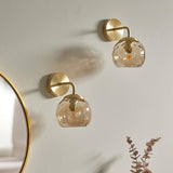 Endon Draycott wall lights in satin brass with champagne dimpled glass globe shades, mounted as a pair on a pale wall beside a round gold-framed mirror.