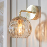 Endon Draycott wall light in satin brass with a champagne lustre dimpled glass globe shade, lit on a panelled wall beside botanical artwork.