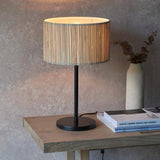 Salcombe Table Lamp with matt black base and stem, woven seagrass drum shade, lit on a wooden console table beside books and a vase.