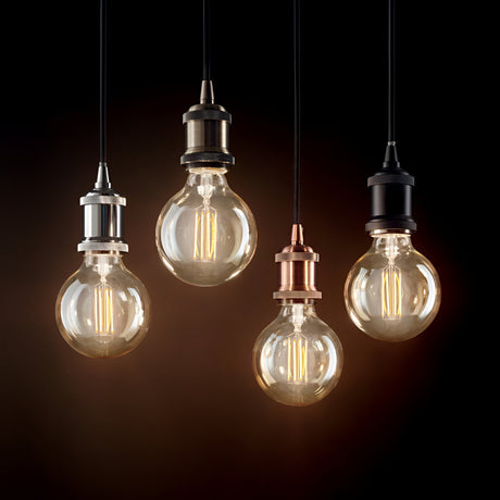 Four vintage-style Zip 1 Light Pendants hang in a row against a dark background, each embodying an industrial style. The pendants feature unique metallic sockets—silver, bronze, copper, and black—highlighting the glowing filaments inside.