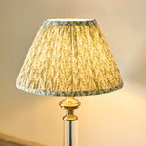 Endon Aldmont Leaf table lamp with a gathered, pleated green leaf-print faux linen shade on an antique brass cap and clear glass column base.