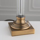 Close-up of Endon Aldmont Leaf table lamp base, showing the clear glass column set on stepped antique brass metalwork and a square plinth.