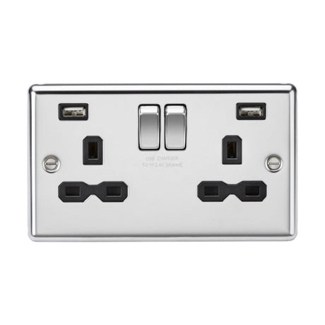 The polished chrome double wall socket, named the 13A 2 Gang SP Switched Socket With Dual USB, boasts a decorative design featuring two UK-style plug outlets and a dual USB charger. Its glossy plate with black insert includes two switches situated above the outlets for convenient control, complemented by its rounded edges.