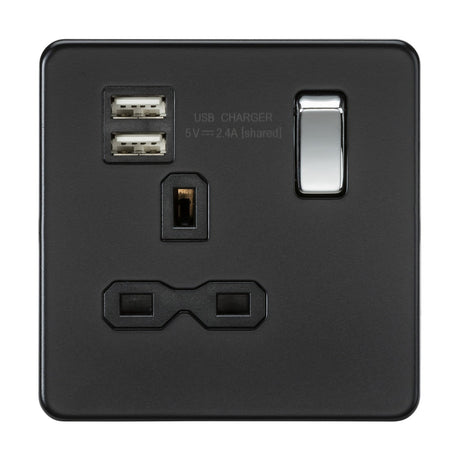 The 13A 1 Gang SP Switched Socket With Dual USB in matt black comes with a chrome rocker and features dual USB charging ports, a single switch, and a standard three-pin plug outlet. It boasts a screwless design for seamless installation, with "USB Charger 5V 2.4A [shared]" labeled above the USB ports.