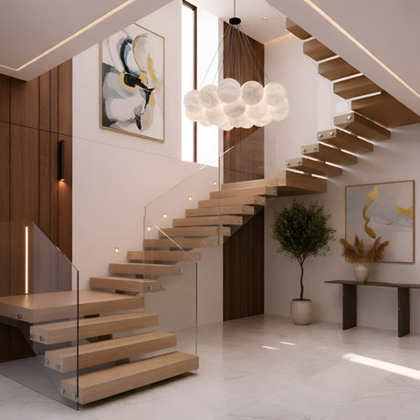 Modern interior with a floating wooden staircase, glass railing, large abstract paintings, a potted tree, decorative console table, and the Auriel 19 Light Alabaster Chandelier in Soft White & Black. Space features light walls and a marble floor.