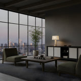 Modern living room with floor-to-ceiling windows, minimalist furniture, a low wooden table with tea set, potted plant, and the Strataform 1 Light Framed Alabaster Table Lamp – Brass & Soft White adding elegant modern lighting on the sideboard.