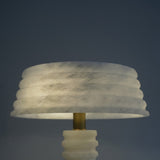 Orivon 3-light sculpted alabaster table lamp with ribbed drum shade and tapered base, joined by a brass finial, glowing warm white against a dark background.
