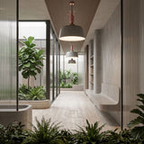 A modern hallway with large glass windows, minimalistic gray walls, built-in bench seating, lush green plants, and natural light. The Bon Light Pendant Light in White adds a contemporary touch to this serene and well-lit space.