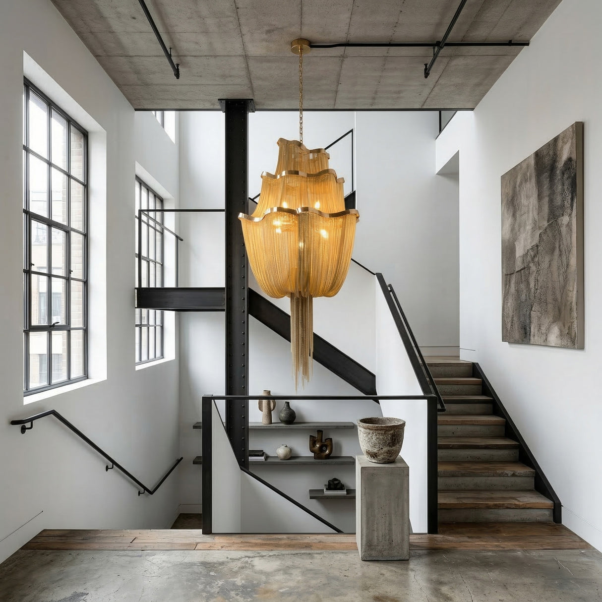 A modern industrial staircase features wooden steps, black railings, large windows, and the Mireya 8 Light Metal Chain Veil Chandelier in gold. Minimalist decor includes pottery on shelves and abstract wall art in a bright, open space.