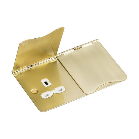 A sleek, rectangular 13A 2 Gang Unswitched Floor Socket in brushed brass with a hinged lid contains a small white object featuring two prongs and an accessory shaped like a ring. The gold-colored case, crafted from premium-grade steel, boasts a smooth, reflective finish that exudes an elegant floor socket design.