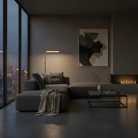 A modern living room at dusk features city views, a gray sectional sofa, abstract wall art, and a minimal coffee table. The Linea LED Alabaster Floor Lamp in brushed brass casts a warm glow over the inviting space.