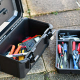 Open AVSL Mercury MTC-41 IP67 waterproof case in matte black holding a multimeter and tools, with removable tray of screwdrivers and pliers on paving.