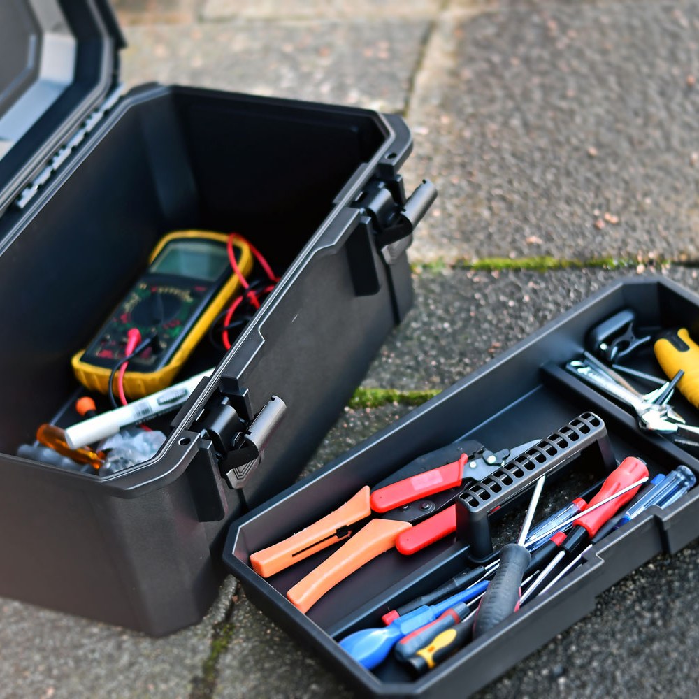 Open Mercury MTC-46 IP67 case by AVSL on paving, showing multimeter and marker inside, with removable tray of pliers, crimper, and screwdrivers beside it.