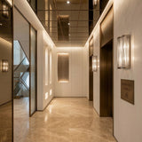 Modern, elegant elevator lobby with marble floors, warm lighting, and sculptural Mireya 6 Light Metal Chain Veil Wall Light - Nickel. Features a mirrored ceiling, two elevators, a sign reading Residences Level 1 A, and a staircase visible through a glass panel.
