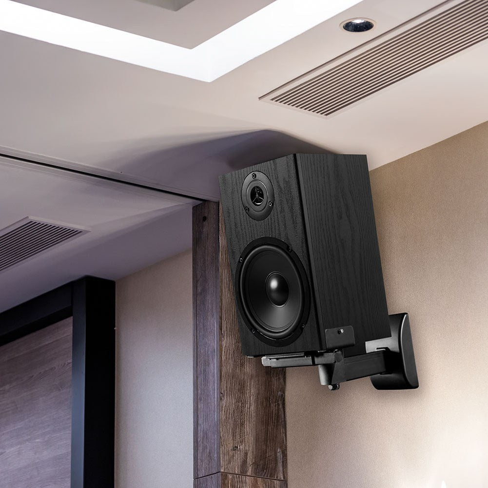 AV:Link universal side clamping speaker wall mount in matt black steel, holding a black bookshelf speaker angled from a wood-panelled corner wall.