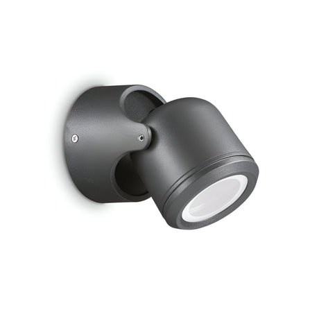 A contemporary black adjustable wall-mounted spotlight, featuring a cylindrical design and IP44 rating, set against a white backdrop. The light is angled downward and mounted on a circular base. Product Name: Vista Outdoor Wall Spotlight - Black.