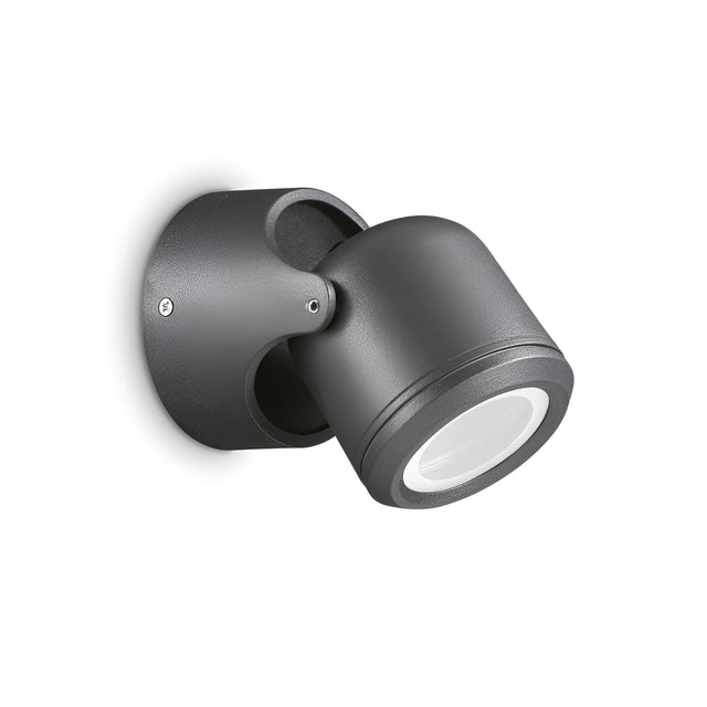 A contemporary black adjustable wall-mounted spotlight, featuring a cylindrical design and IP44 rating, set against a white backdrop. The light is angled downward and mounted on a circular base. Product Name: Vista Outdoor Wall Spotlight - Black.