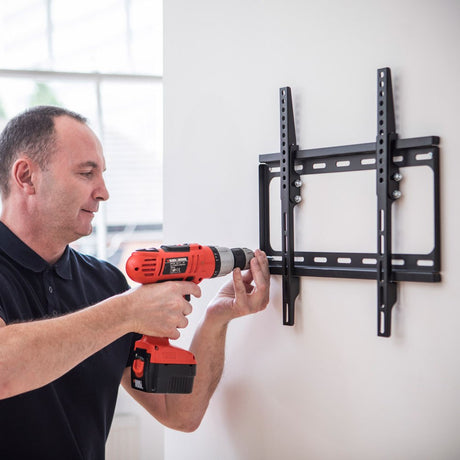 Man using a cordless drill to install the AVSL AV:Link ST401 tilting TV wall bracket, a matte black VESA 400x400 mount, on a white wall.