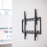 AV:Link ST401 tilting TV wall bracket in matte black steel on a white wall, showing the low-profile VESA 400x400 frame with vertical arms and fixing bolts.