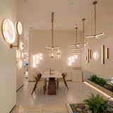 Elvaris LED Small Vertical Alabaster Wall Light in Brushed Brass, shown illuminated on a dining room wall alongside pendant lights and wall art.