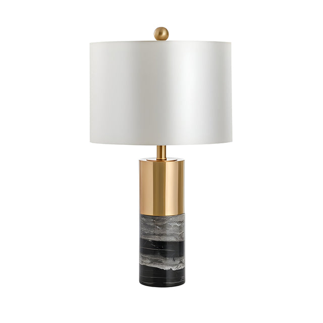 The Valmora 1 Light Monolith Marble Table Lamp features a black and white marble-patterned base, brass accents, a white cylindrical shade, and is topped with a round gold finial for a modern touch.