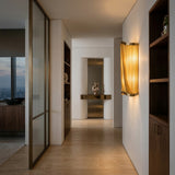 A modern hallway with neutral tones, the Mireya 6 Light Metal Chain Veil Wall Light in gold, luxury wall decor, built-in shelves, and a sculptural centerpiece on a console table. Large windows frame a city view in the background.