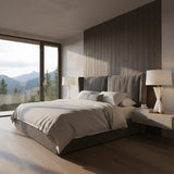 A modern bedroom with a large bed, two white bedside tables topped with Astren 1 Light Crossed Alabaster Table Lamps in Brushed Brass & Soft White. Light wood floors and floor-to-ceiling windows fill the minimalist space with natural light and mountain views.