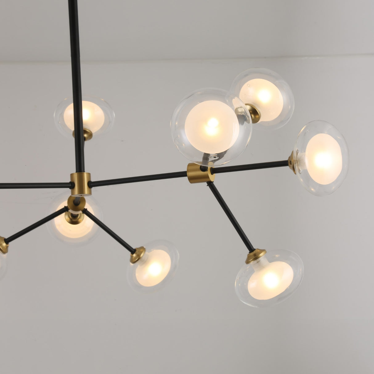 The Galaxy 12 Light Chandelier - Black & White is a modern fixture with twelve round glass globes on black and brass arms, suspended from a white ceiling. It emits a soft, warm glow for a starburst-inspired look.