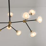 The Galaxy 12 Light Chandelier - Black & White is a modern fixture with twelve round glass globes on black and brass arms, suspended from a white ceiling. It emits a soft, warm glow for a starburst-inspired look.