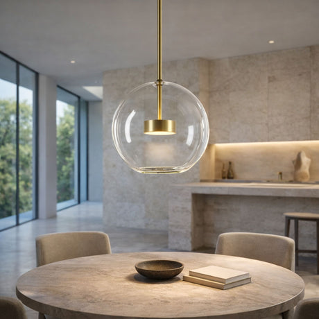 A modern dining area features a round table, four beige chairs, a bowl, and books. The Bubble LED Glass Pendant Light - Gold with its minimalist design hangs above, while a stone kitchen and large windows create a bright, airy space.