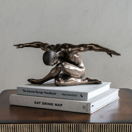 Libra Interiors Bronze Male Arms Outstretched Sculpture on stacked design books atop a dark wood console against a neutral wall.