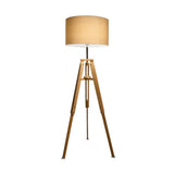 The Gaia Wood Floor Lamp - Light Brown showcases a natural wood tripod base paired with a beige cylindrical fabric shade, offering rustic charm.