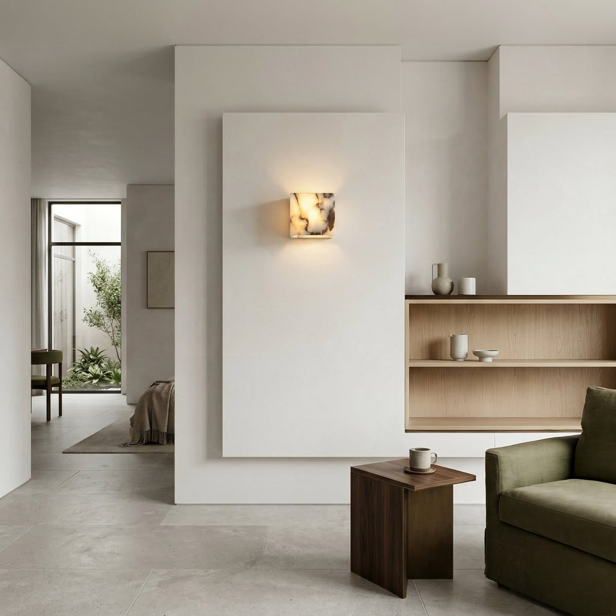Minimalist living room with light beige walls, open wooden shelves, a small wooden side table with a mug, and a green sofa. Sunlight highlights the Alvara 1 Light Cube Veined Marble Wall Light in white & black near the open doorway.