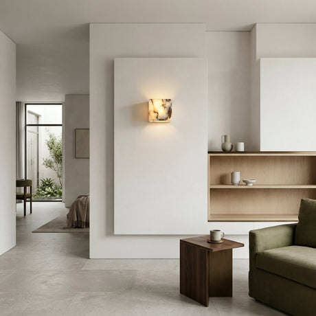 Minimalist living room with light beige walls, open wooden shelves, a small wooden side table with a mug, and a green sofa. Sunlight highlights the Alvara 1 Light Cube Veined Marble Wall Light in white & black near the open doorway.