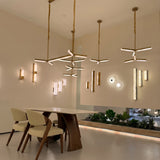 Elvaris LED Small Vertical Alabaster Wall Light in Brushed Brass, shown illuminated among pendant and wall lights in a dining room setting with wooden table and chairs.