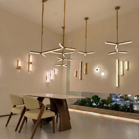 Elvaris LED Small Vertical Alabaster Wall Light in Brushed Brass, shown illuminated among pendant and wall lights in a dining room setting with wooden table and chairs.