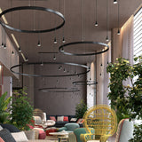 Skybell Circle Iron Ring LED Pendant Light in Ebony Black, multiple black rings with hanging cone-shaped LED heads, shown in a modern living space with sofas and greenery.