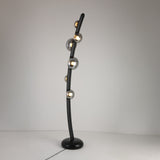 The Cordaro 6 Light Leather Floor Lamp in Black features six spherical bulbs with metallic finishes on a curved black stand and round base, shown against a plain white background.
