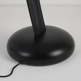 A close-up of the round, black base of the Cordaro 6 Light Leather Floor Lamp - Black, with a black electric cord extending from the bottom across a white surface.