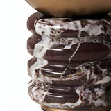 A close-up of the Caldris 1 Light Sculpted Marble Table Lamp in brass atop a purple red marble pedestal with rich veining and glossy texture.