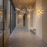 Niori Bubble 3 Light LED Glass Linear Pendants in gold illuminate a modern hallway with travertine walls, a built-in bench, and floor-to-ceiling windows.